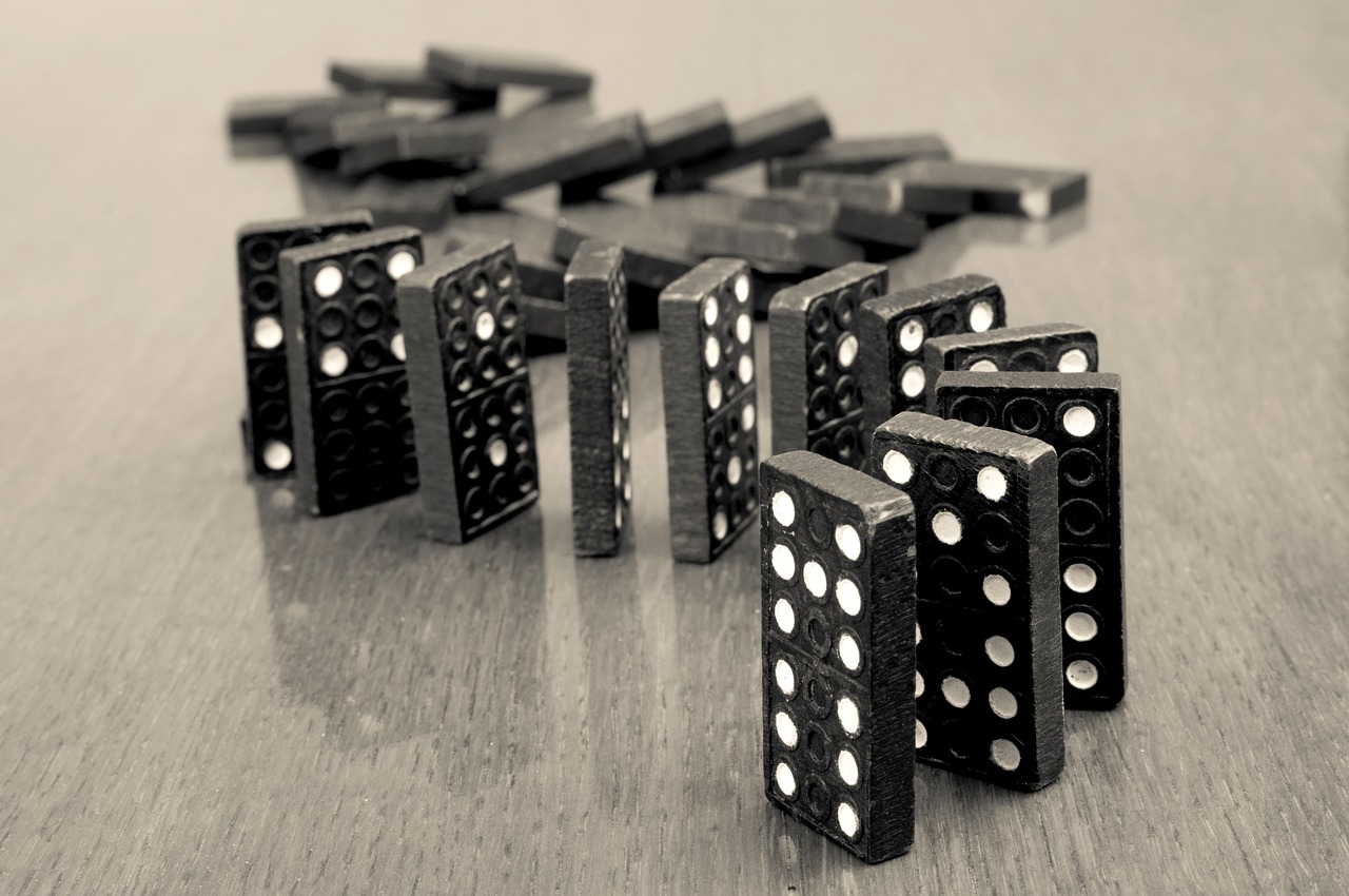 Close-up of black domino pieces standing on a wooden surface, with some dominoes lying flat in the background, photographed in black and white.